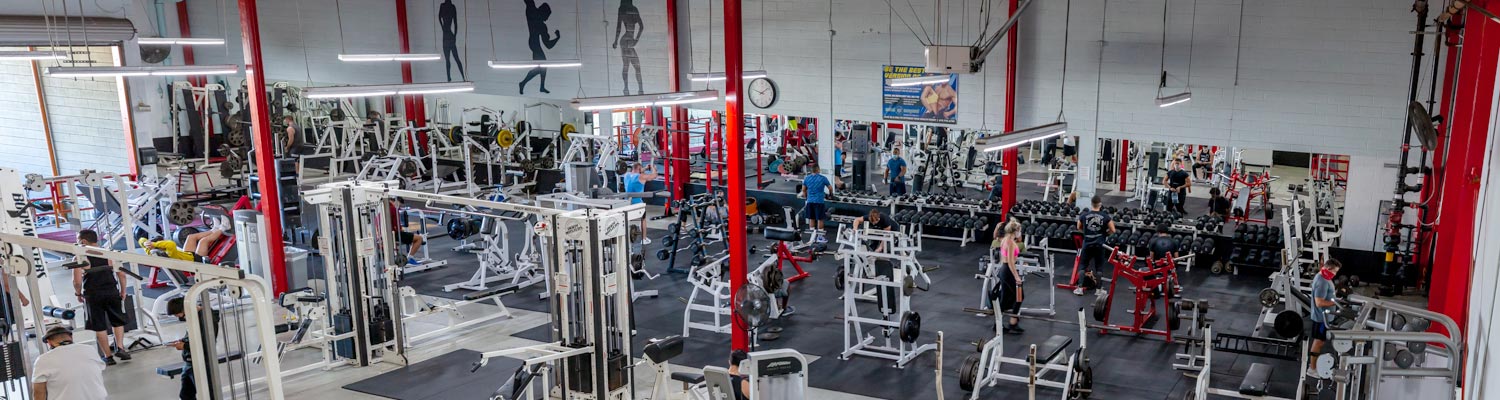 The full Boulevard Fitness floor, with free weights, benches and machines under red steel beams